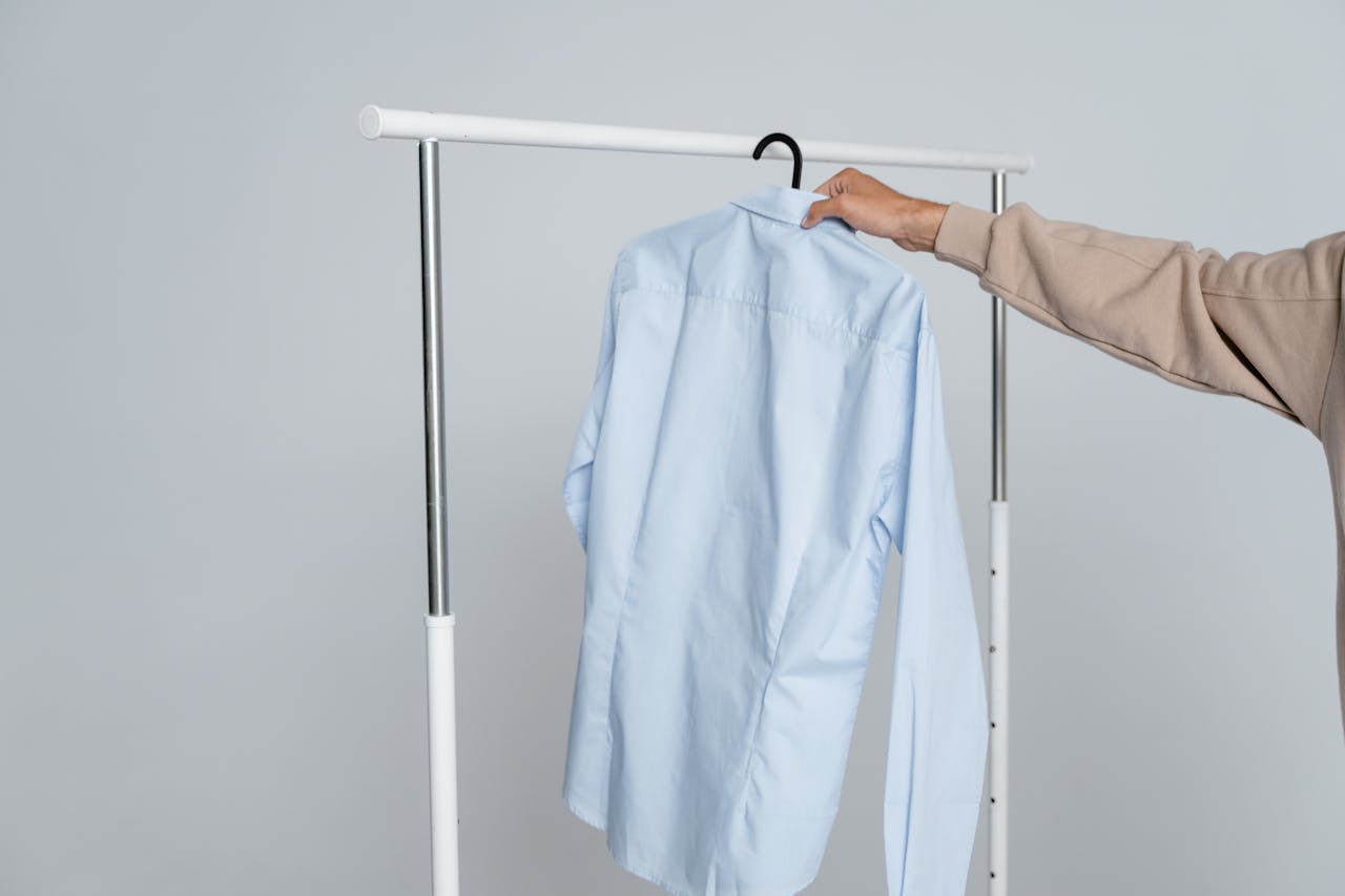 A person holding a blue shirt on a rack against a neutral background.