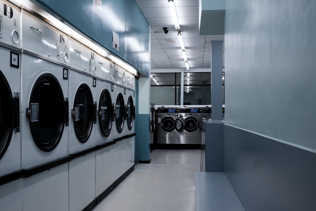 Local launderette business at night time, lots of washing machines and tumble dryers. An empty store illuminated by fluorescent light in Bristol, UK. 2/5